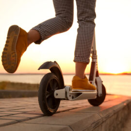 Woman riding electric kick scooter outdoors at sunset