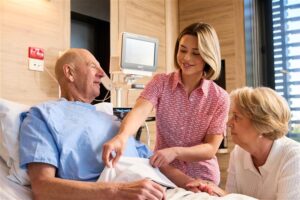 Cabrini nurse assisting a male patient in bed with their partner sitting near by