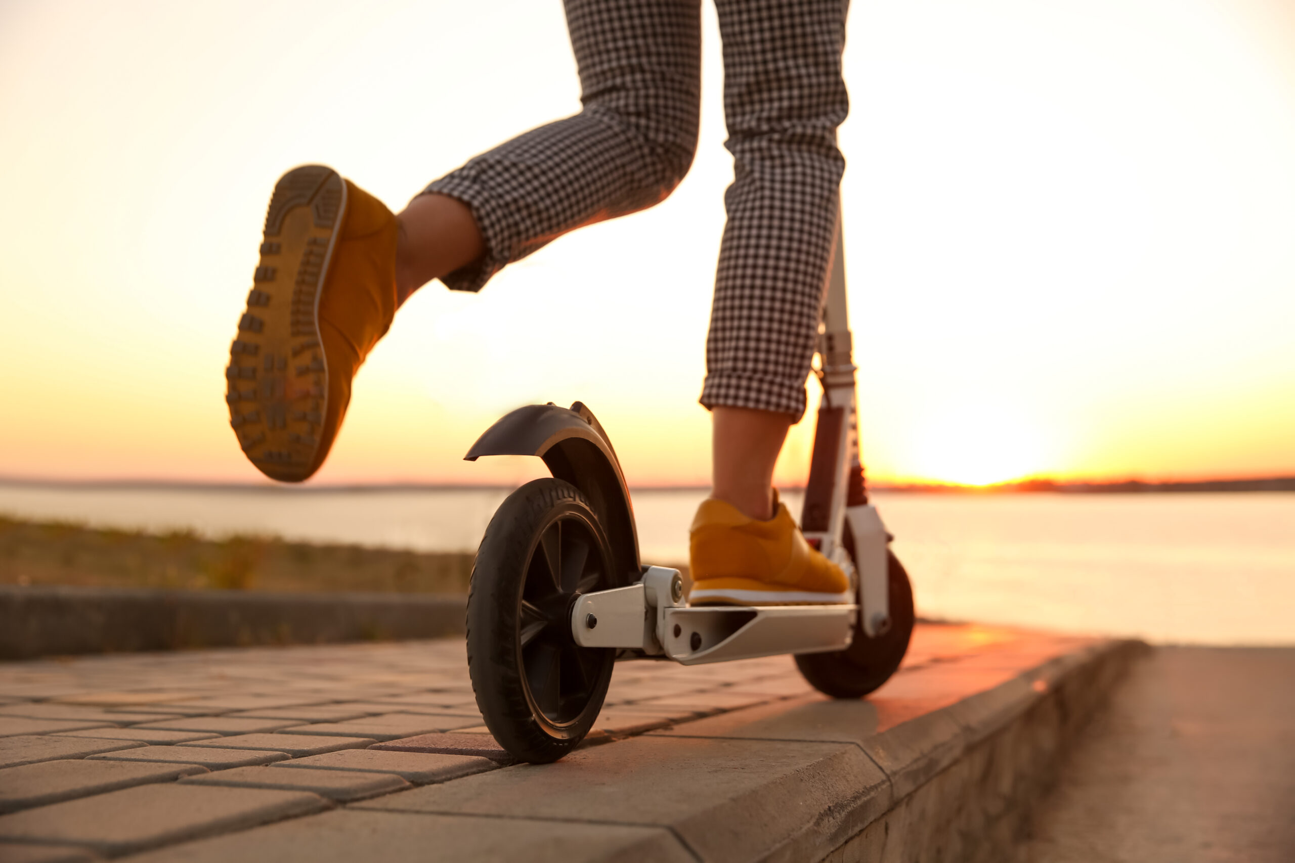 Woman riding electric kick scooter outdoors at sunset