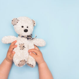 two kid hands hold a small toy teddy bear on a blue background,