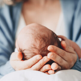 Newborn on mother's knee with mother's hands holding their head