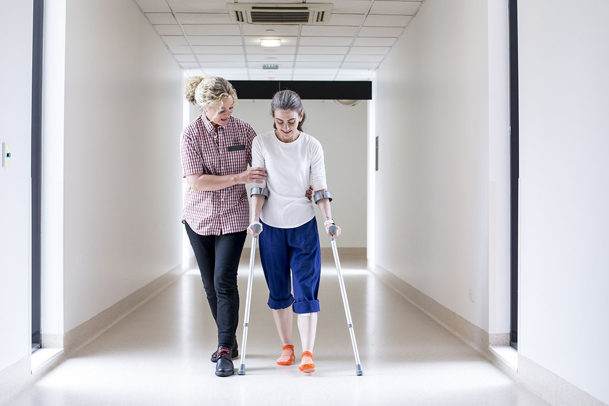 Orthopaedic patient walking on crutches, with the aid a Cabrini nurse